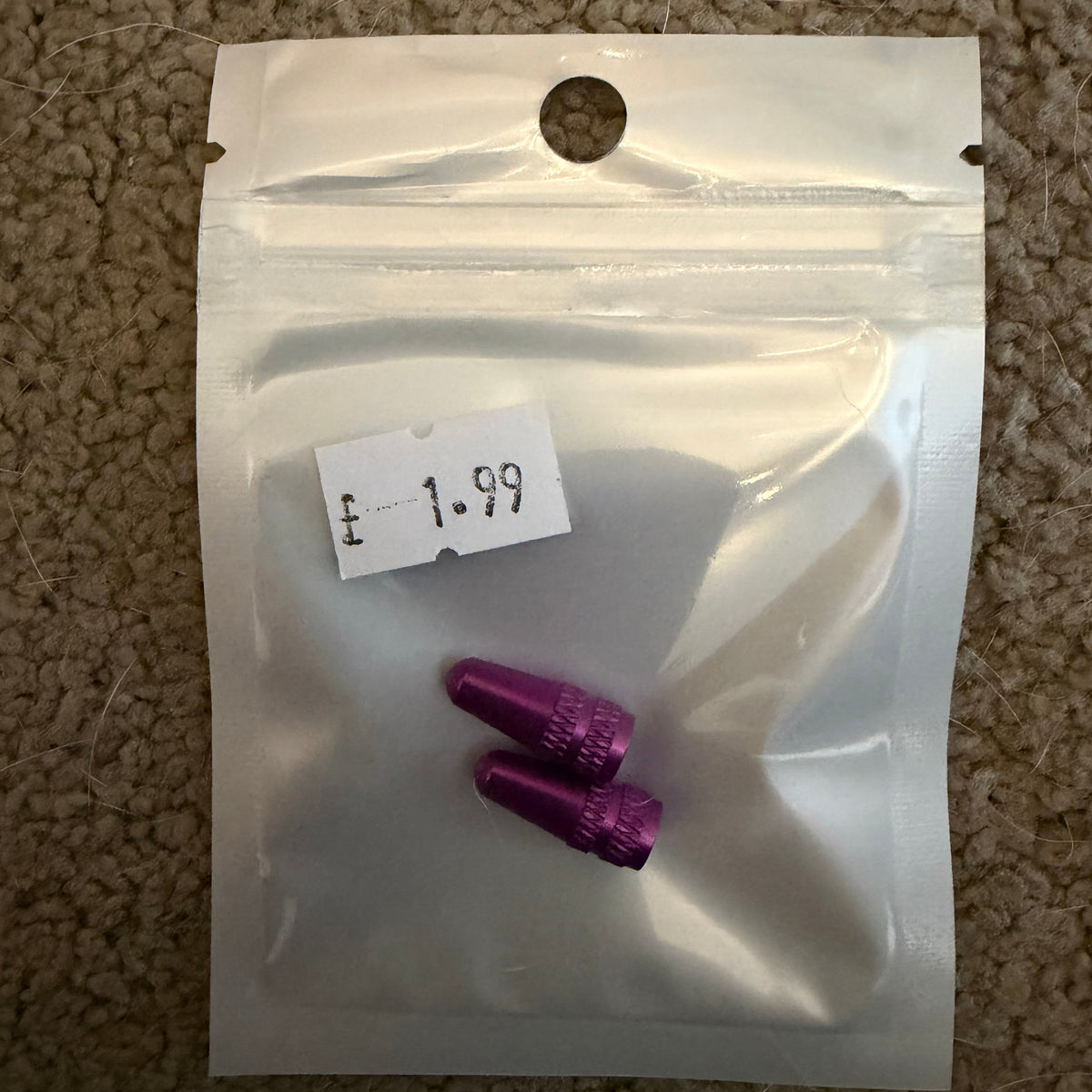 Aluminium Presta Valve Caps, purple cylindrical caps with knurled texture, displayed inside a clear bag on a gray carpet.