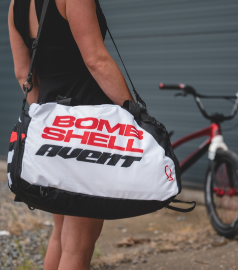 Bombshell Training Kit Bag in white with bold red and black text, rectangular duffel shape, black straps and side pockets.
