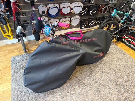 Bombshell Bike Bag by SSS Racing, black durable fabric with pink handles and zipper, shown beside teal mountain bike in.