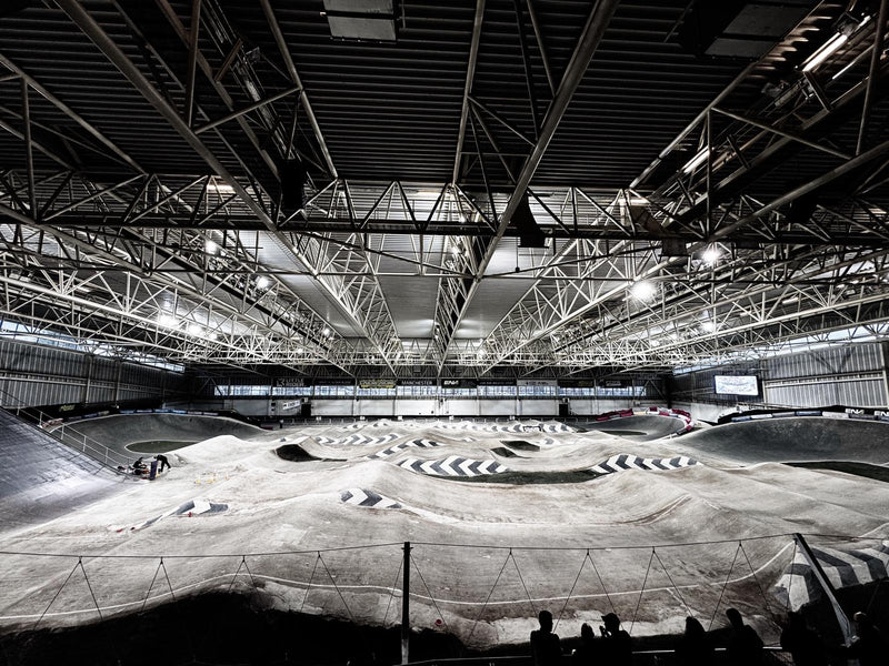 Indoor BMX racing track with geometric patterns on the ground, large indoor arena with high ceilings.