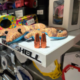 Aluminium Presta Valve Caps in copper-orange finish, conical tops standing upright on shelf with blurred boxes. Set on shelf.
