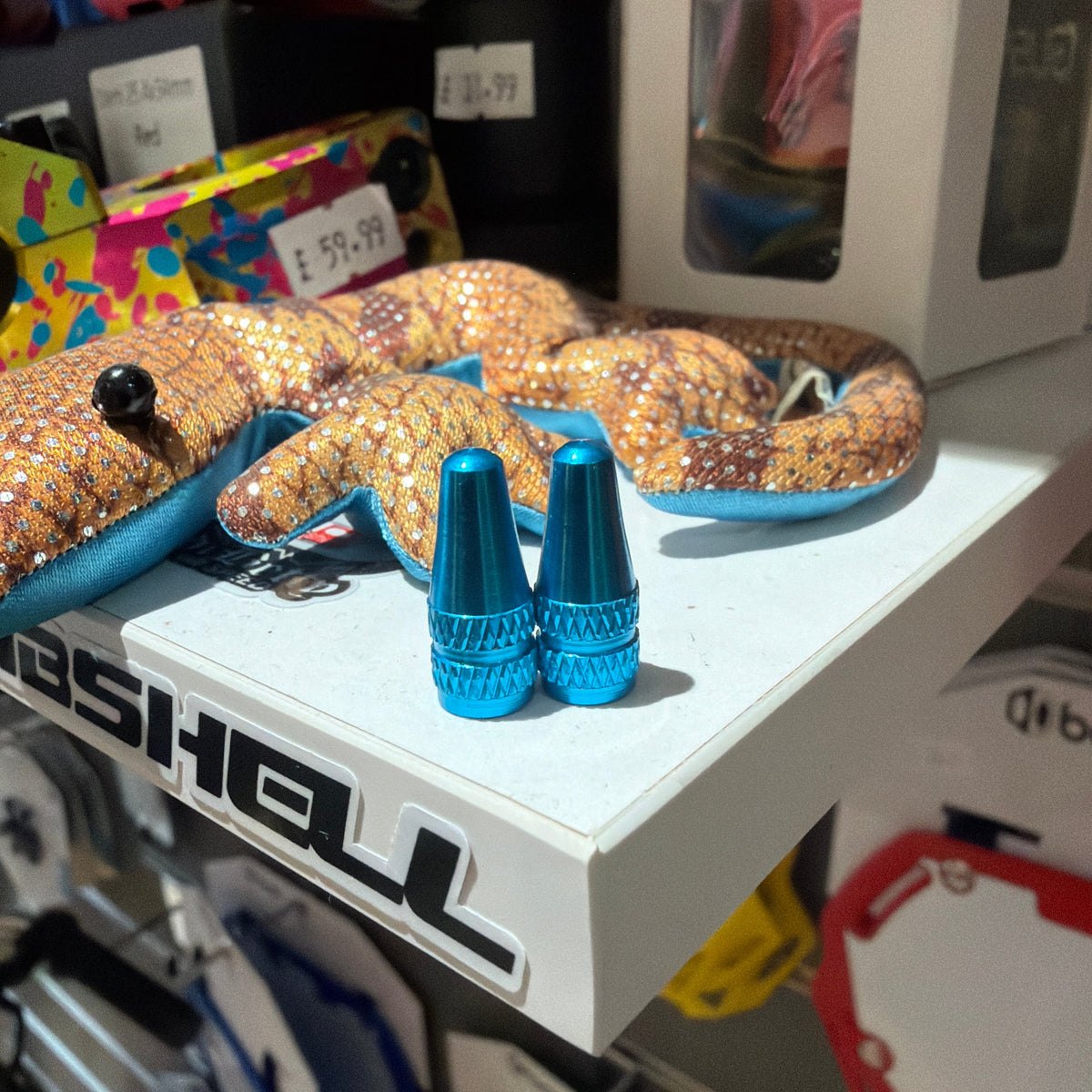 Aluminium Presta Valve Caps in bright blue, cone shaped with knurled facets and glossy finish displayed atop a shelf now.