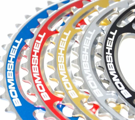 Bombshell Chainring by SSS Racing in blue, red, gold, silver, and black aluminum alloy, rugged teeth, bold BOMBSHELL branding