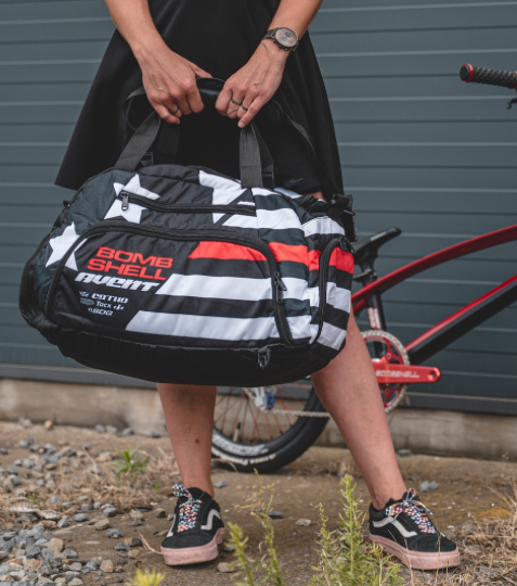 Bombshell Training Kit Bag in black with white stripes and red panel, oval duffel shape carried by two handles and durable