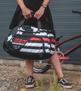 Bombshell Training Kit Bag in black with white stripes and red panel, oval duffel shape carried by two handles and durable